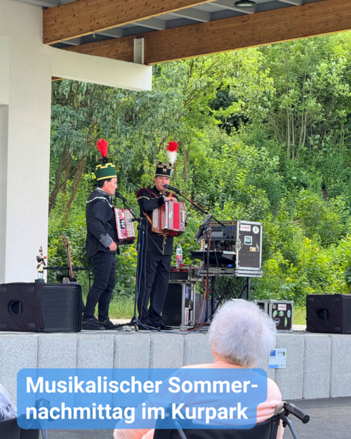 wei Musiker in Trachten spielen Akkordeon auf einer Bühne im Freien vor Zuschauern. Text: 'Musikalischer Sommernachmittag im Kurpark'
